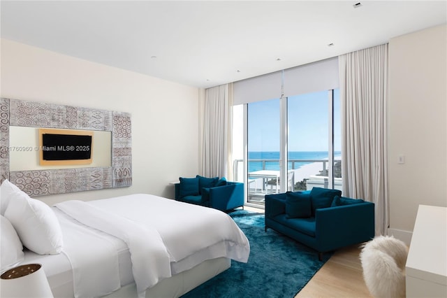 bedroom featuring access to outside, wood finished floors, and a water view