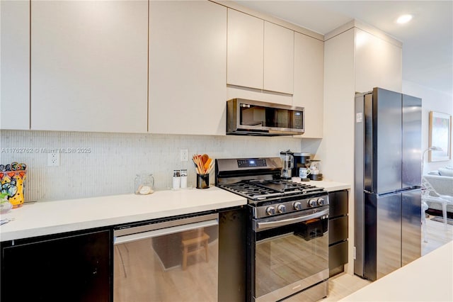 kitchen with modern cabinets, cream cabinets, stainless steel appliances, light countertops, and decorative backsplash