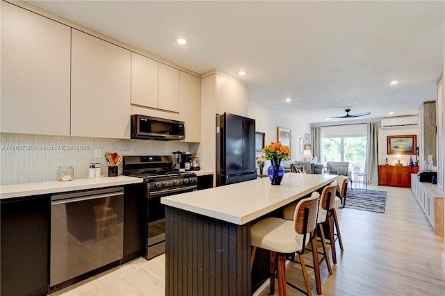 kitchen with a wall mounted AC, light countertops, appliances with stainless steel finishes, a kitchen bar, and a center island