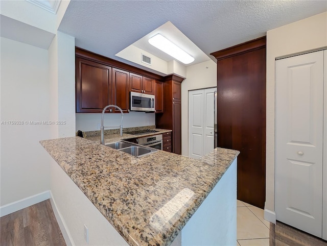 kitchen with a sink, light stone counters, a textured ceiling, appliances with stainless steel finishes, and a peninsula