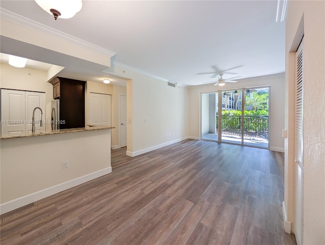 unfurnished living room featuring wood finished floors, baseboards, a sink, ceiling fan, and ornamental molding