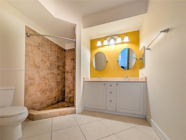 bathroom with toilet, a sink, a tile shower, double vanity, and baseboards