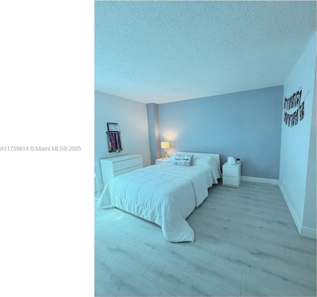 bedroom with baseboards, light wood-type flooring, and a textured ceiling