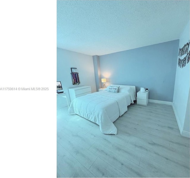 bedroom with light wood finished floors, a textured ceiling, and baseboards