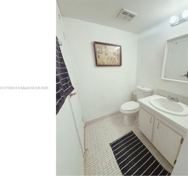 half bathroom featuring vanity, baseboards, visible vents, tile patterned flooring, and toilet