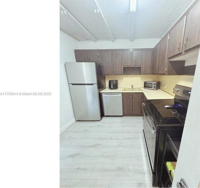 kitchen with baseboards, a sink, light countertops, appliances with stainless steel finishes, and light wood-type flooring