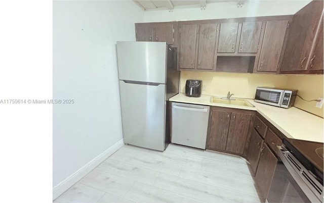 kitchen with a sink, stainless steel appliances, light countertops, baseboards, and dark brown cabinets