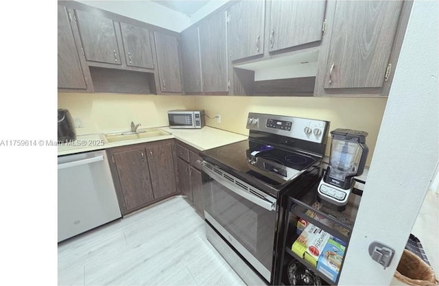 kitchen with a sink, under cabinet range hood, appliances with stainless steel finishes, light wood finished floors, and light countertops