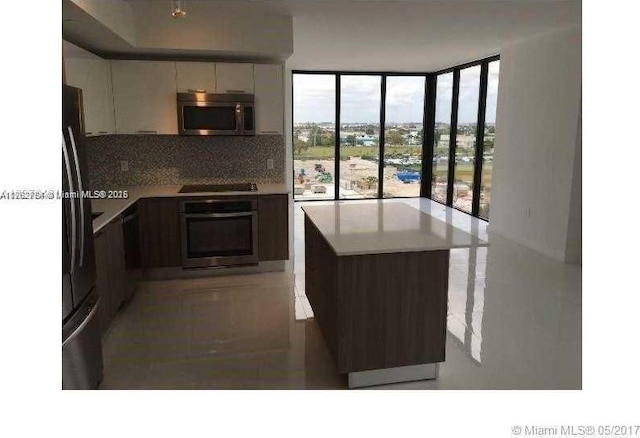 kitchen featuring black appliances, tasteful backsplash, white cabinets, light countertops, and a wall of windows