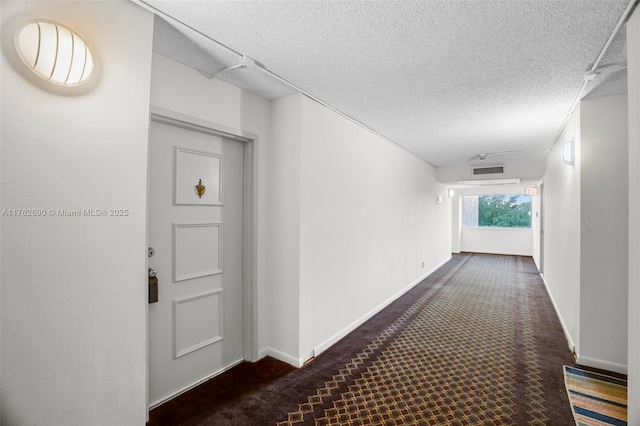 hallway with a textured ceiling, baseboards, and carpet floors