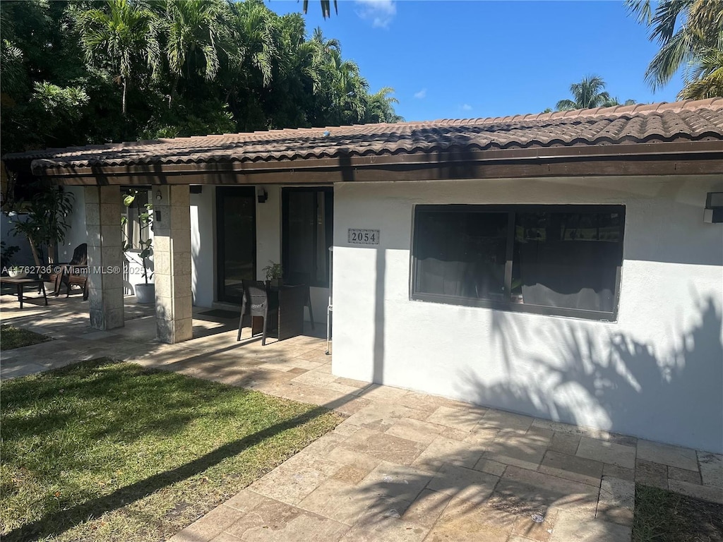 exterior space with stucco siding, a tile roof, and a patio