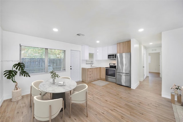 kitchen with light countertops, light wood-style flooring, appliances with stainless steel finishes, modern cabinets, and a sink