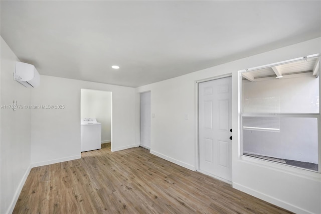 spare room featuring an AC wall unit, baseboards, washer / dryer, and wood finished floors