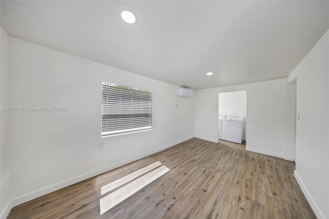 unfurnished room with washer and clothes dryer, a wall mounted air conditioner, baseboards, and wood finished floors