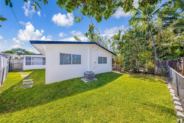 rear view of house featuring stucco siding, cooling unit, a yard, and a fenced backyard