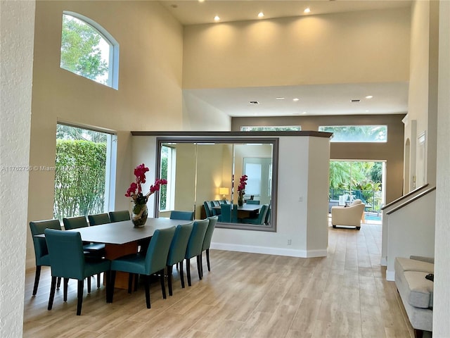 dining space featuring recessed lighting, light wood-style flooring, a high ceiling, and baseboards