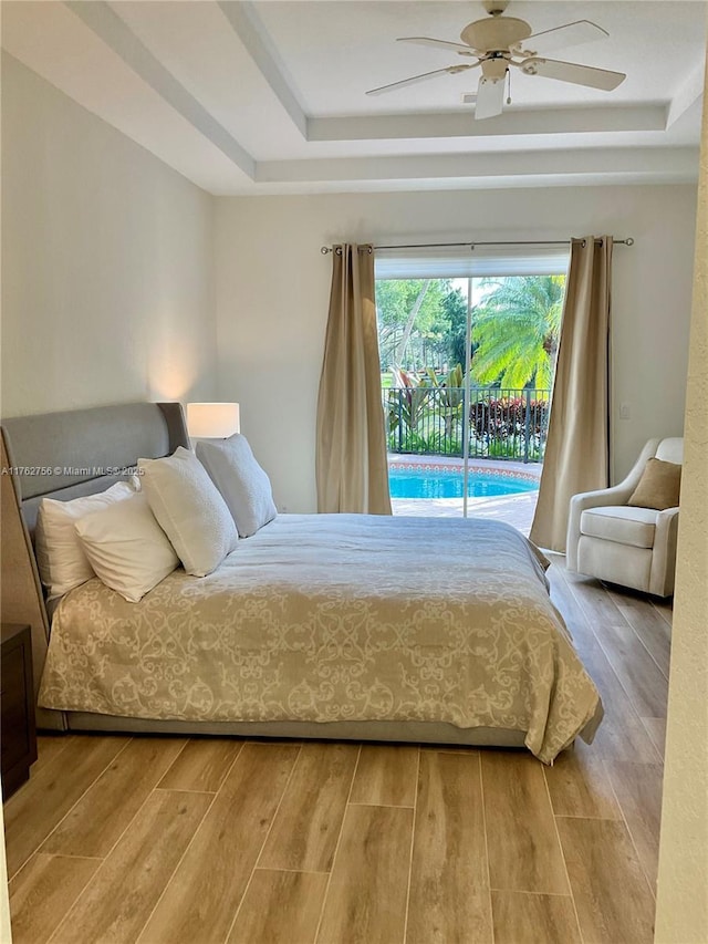 bedroom featuring a tray ceiling, wood finished floors, a ceiling fan, and access to outside