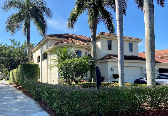 mediterranean / spanish-style house featuring stucco siding, an attached garage, and a tile roof