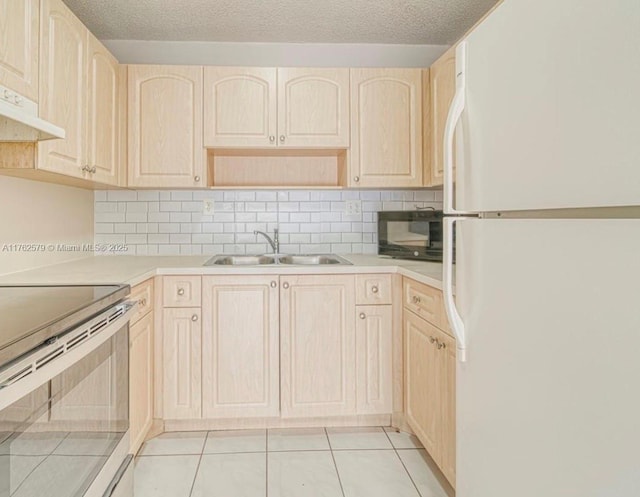 kitchen with a sink, black microwave, freestanding refrigerator, and light brown cabinetry