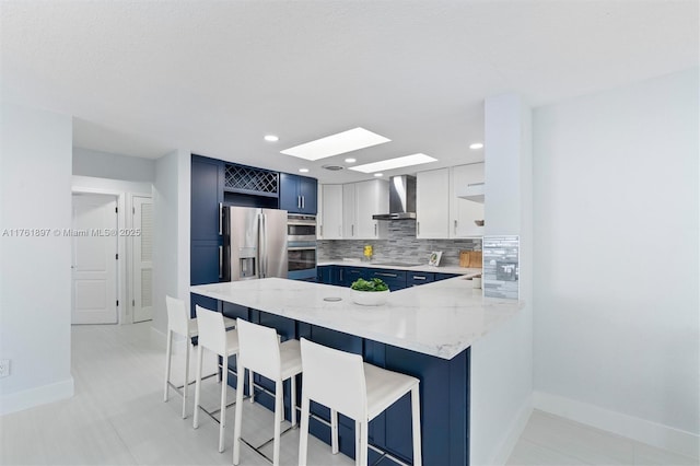 kitchen with blue cabinets, appliances with stainless steel finishes, a peninsula, wall chimney exhaust hood, and open shelves