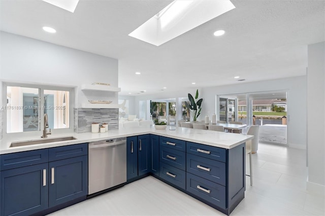 kitchen featuring a peninsula, a skylight, a sink, stainless steel dishwasher, and backsplash