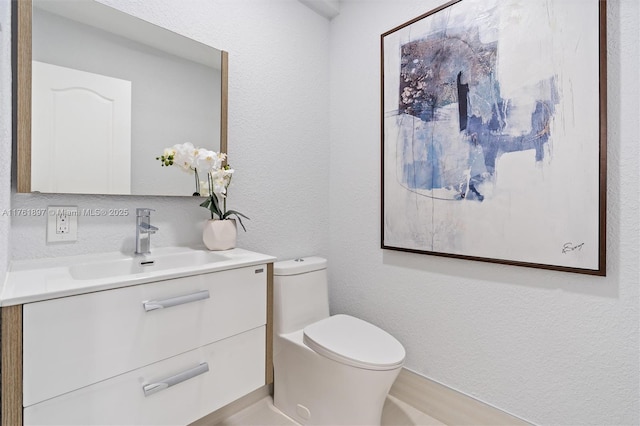 half bath featuring toilet, vanity, and a textured wall