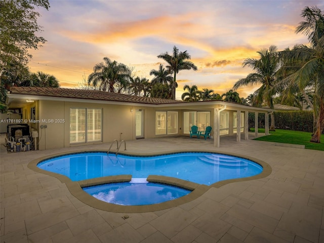 pool at dusk with a patio area, an outdoor pool, and an in ground hot tub