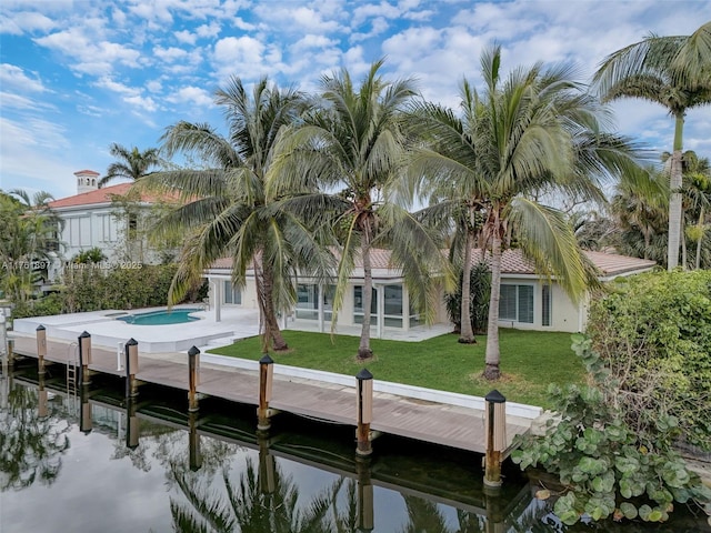 back of house with an outdoor pool, stucco siding, a water view, and a lawn