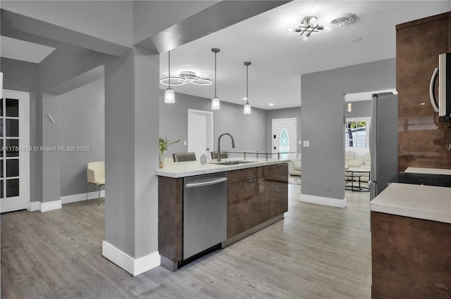 kitchen featuring light wood finished floors, dark brown cabinets, light countertops, appliances with stainless steel finishes, and a sink