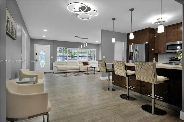 kitchen with dark brown cabinetry, light countertops, a kitchen bar, appliances with stainless steel finishes, and wood finished floors