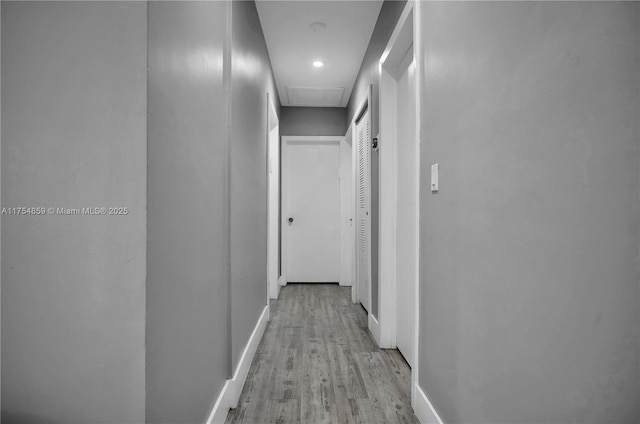 hall featuring light wood finished floors, attic access, and baseboards