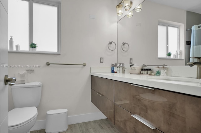 bathroom with toilet, vanity, baseboards, and wood finished floors