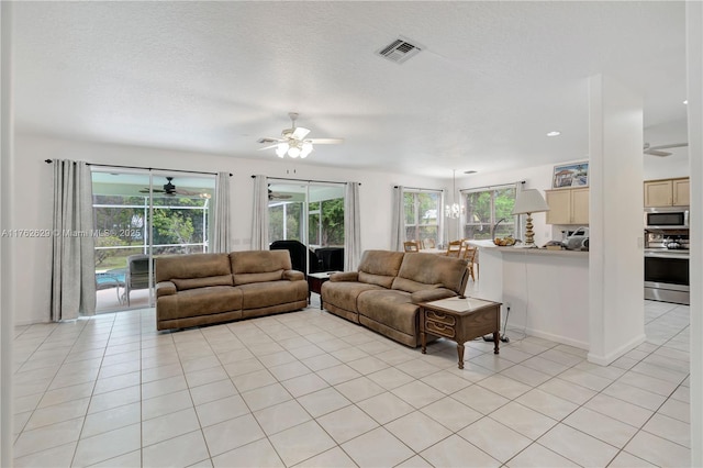 living area featuring visible vents, a textured ceiling, light tile patterned flooring, baseboards, and ceiling fan