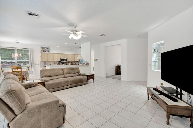 living area featuring light tile patterned floors, visible vents, and ceiling fan with notable chandelier