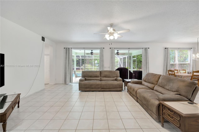 living area featuring light tile patterned floors, ceiling fan with notable chandelier, and a textured ceiling