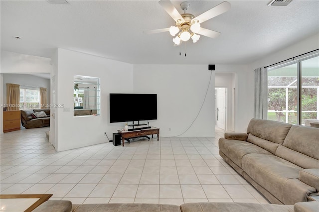 living room featuring light tile patterned floors, visible vents, a textured ceiling, and a ceiling fan