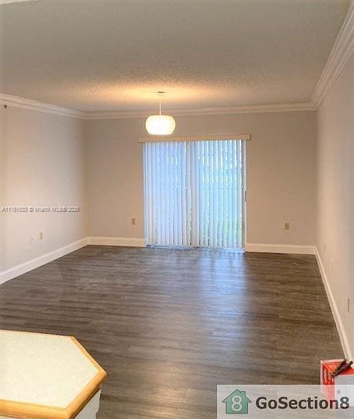 spare room featuring crown molding, dark wood-style floors, baseboards, and a textured ceiling