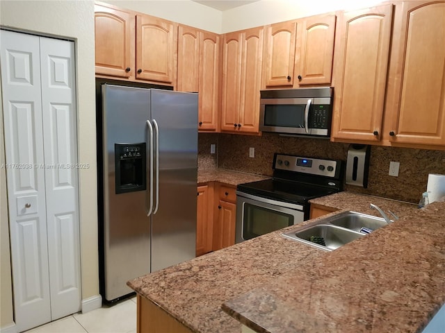 kitchen with a sink, stone counters, backsplash, and stainless steel appliances