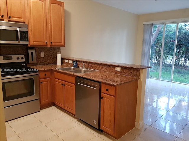 kitchen featuring a sink, dark stone countertops, appliances with stainless steel finishes, a peninsula, and decorative backsplash