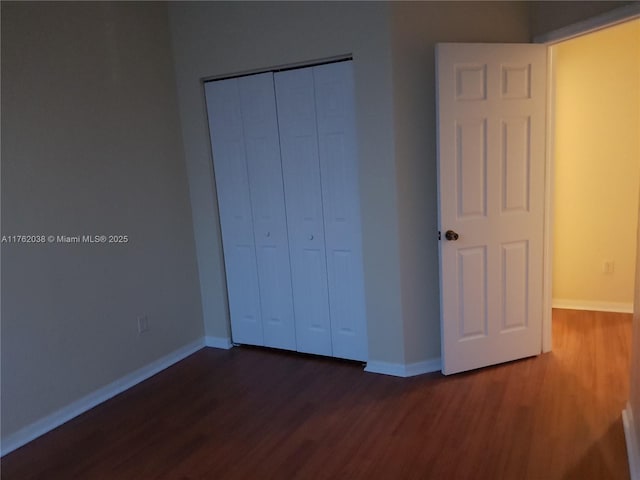 unfurnished bedroom featuring a closet, baseboards, and dark wood-type flooring