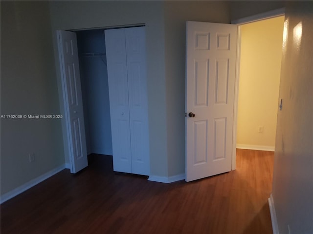 unfurnished bedroom with a closet, baseboards, and dark wood-type flooring