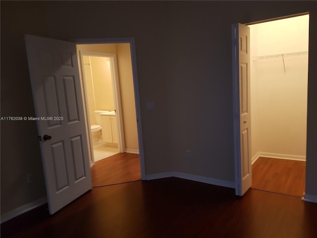 unfurnished bedroom with a closet, connected bathroom, baseboards, and wood finished floors