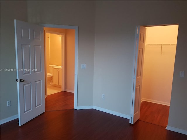 unfurnished bedroom with a walk in closet, baseboards, a closet, and wood finished floors