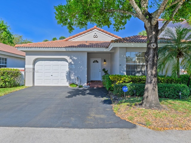 mediterranean / spanish home with aphalt driveway, an attached garage, a tile roof, and stucco siding