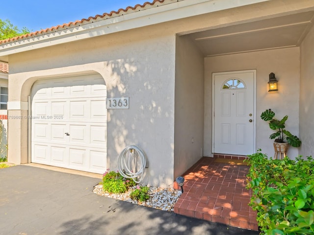 doorway to property with a tile roof, a garage, driveway, and stucco siding