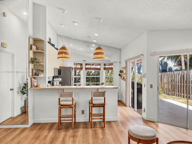 kitchen with light wood finished floors, a kitchen bar, a textured ceiling, and freestanding refrigerator