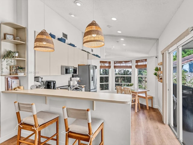 kitchen featuring a breakfast bar area, light countertops, light wood-style flooring, a peninsula, and stainless steel appliances