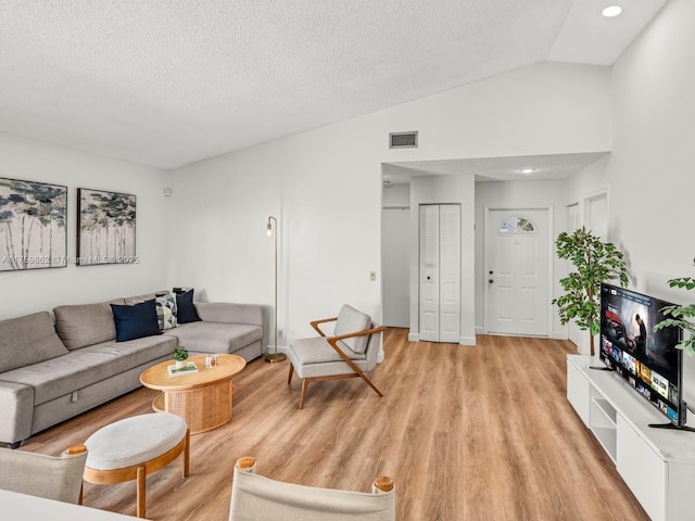 living room with a textured ceiling, lofted ceiling, visible vents, and light wood-type flooring