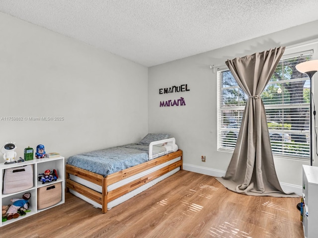 bedroom with light wood-style flooring, multiple windows, baseboards, and a textured ceiling