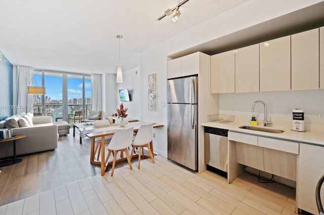 kitchen with light wood finished floors, a sink, floor to ceiling windows, stainless steel appliances, and light countertops